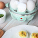 Egg cooker power indicator light is lit red. Plate of deviled eggs next to egg cooker.