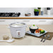 Rice cooker display on kitchen counter with cooked white rice inside pot.  Next to a plate of prepared food, rice and vegetables.